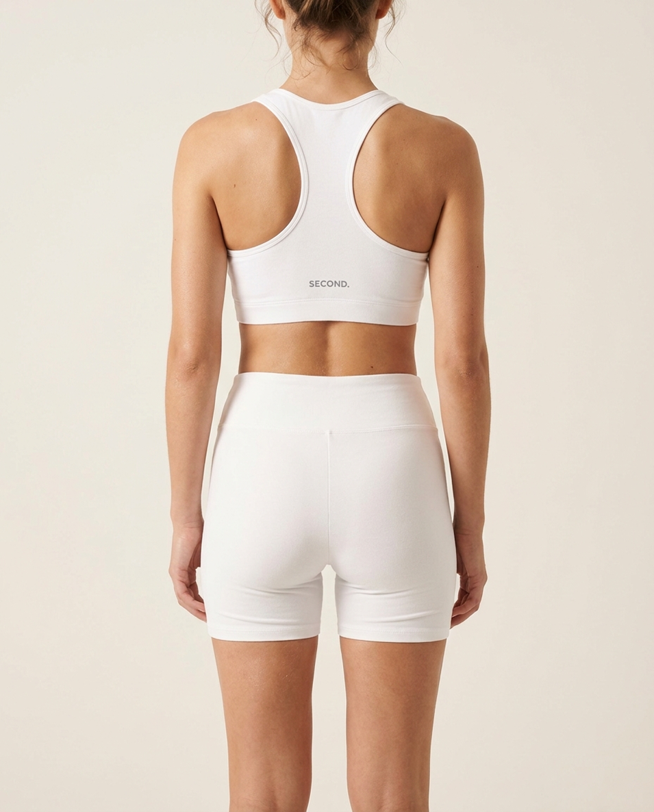 Woman wearing the SECOND. organic cotton activewear set in white on a bone studio background