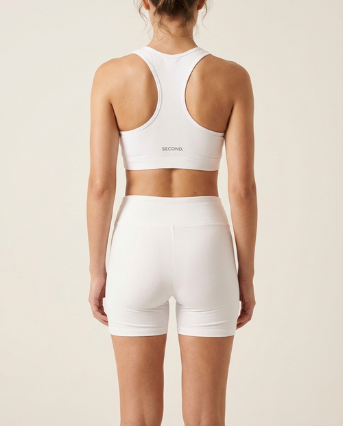 Woman wearing the SECOND. organic cotton activewear set in white on a bone studio background